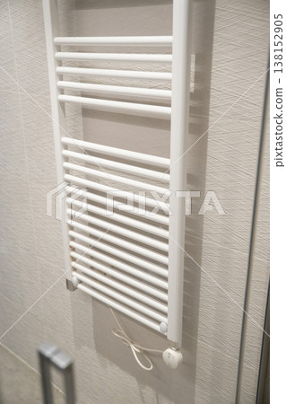 White electric towel radiator mounted on textured bathroom wall, providing warmth and comfort in a modern home, improving daily life and hygiene White electric towel radiator mounted on textured bathroom wall, providing warmth and comfort in a modern home, improving daily life and hygiene 138152905
