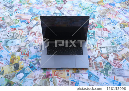 Modern laptop lies on big amount of money bills banknotes from different currencies close up 138152998