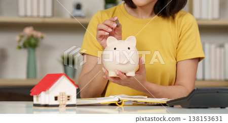 Woman saving money into a piggy bank Woman saving money into a piggy bank 138153631