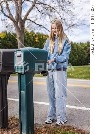 Young woman opening mailbox on suburban roadside in United States residential neighborhood Young woman opening mailbox on suburban roadside in United States residential neighborhood 138153885