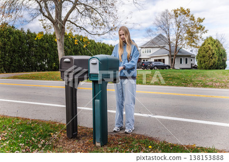 Young woman checking roadside mailbox in suburban United States neighborhood near residential house Young woman checking roadside mailbox in suburban United States neighborhood near residential house 138153888
