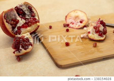 Cut pomegranate on cutting board with scattered arils Cut pomegranate on cutting board with scattered arils 138154028