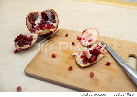 Cut pomegranate on cutting board with scattered arils Cut pomegranate on cutting board with scattered arils 138154029