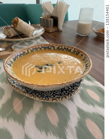 Bowl of creamy soup with pumpkin seeds on wooden table in cozy restaurant setting Bowl of creamy soup with pumpkin seeds on wooden table in cozy restaurant setting 138154401