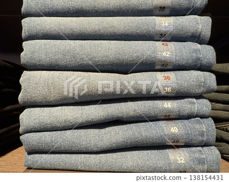Stack of folded blue jeans in various sizes in retail setting with visible size labels Stack of folded blue jeans in various sizes in retail setting with visible size labels 138154431