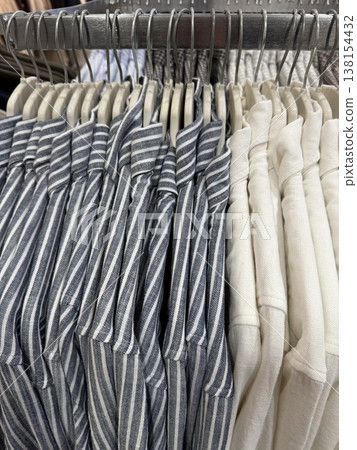 Stacked folded shirts in neutral and striped patterns on metal rack in retail store setting 138154432