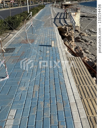 Blue brick sidewalk near rocky beach with weathered texture in coastal environment, background 138154436
