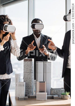 Three professionals in suits wearing VR headsets interact with a miniature city model, exploring architectural designs in a virtual environment 138155614