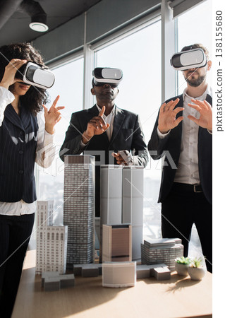 Three professionals wearing VR headsets interact with architectural models, exploring virtual designs in a modern office setting Three professionals wearing VR headsets interact with architectural models, exploring virtual designs in a modern office setting 138155680