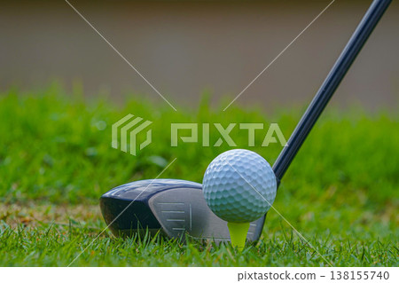 Golf club and golf ball on tee close up in grass field with morning sunshine. 138155740
