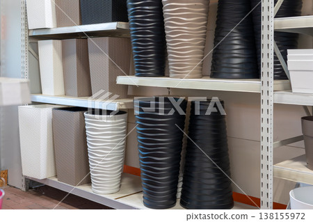 Various contemporary plastic planters with textured surfaces and matte finishes arranged on white shelves in a garden center or home improvement store, ready for purchase 138155972