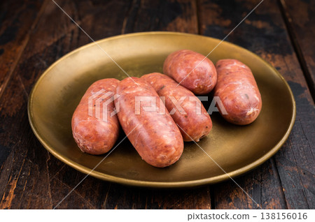 Raw pork sausage links with fresh herbs on rustic plate, traditional butcher style fresh meat product on wooden background. Raw pork sausage links with fresh herbs on rustic plate, traditional butcher style fresh meat product on wooden background. 138156016