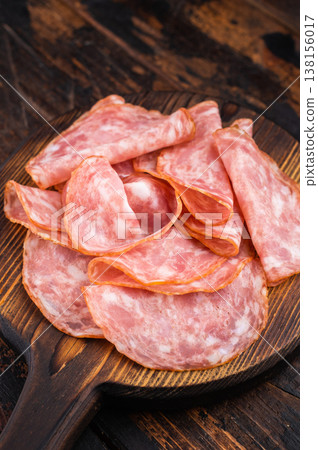 Italian salami sausage slices on wooden board with rosemary on dark wooden background. Rustic charcuterie appetizer with copy space. Italian salami sausage slices on wooden board with rosemary on dark wooden background. Rustic charcuterie appetizer with copy space. 138156017