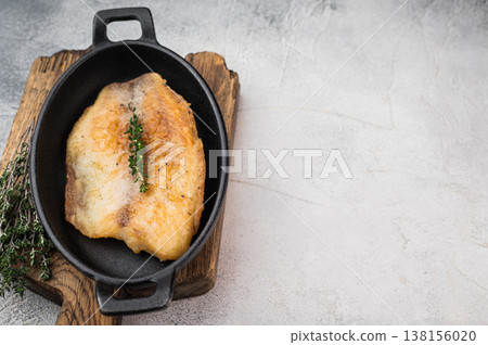 Pan fried tilapia fillet served in small cast iron skillet with thyme on wooden board over light background with copy space. Pan fried tilapia fillet served in small cast iron skillet with thyme on wooden board over light background with copy space. 138156020