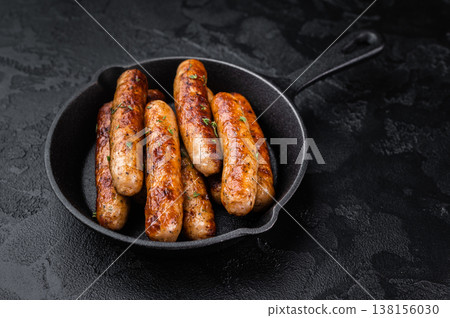 Fried sausage links in black cast iron pan. Golden browned pork sausages on dark rustic background perfect for meal serving. Fried sausage links in black cast iron pan. Golden browned pork sausages on dark rustic background perfect for meal serving. 138156030