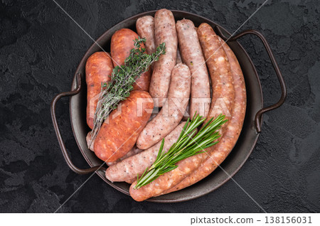Raw sausage assortment in metal pan on dark kitchen background. Fresh pork meat links ready for grilling barbecue preparation. 138156031
