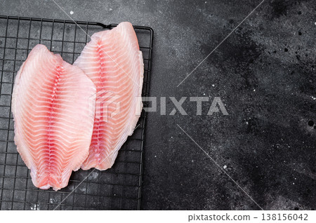 Raw tilapia fillets on metal rack on dark background, aquaculture white fish ingredient. Raw tilapia fillets on metal rack on dark background, aquaculture white fish ingredient. 138156042