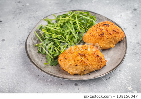 Crispy breaded chicken cutlet stuffed chicken with garlic butter filling served with arugula on gray background Crispy breaded chicken cutlet stuffed chicken with garlic butter filling served with arugula on gray background 138156047