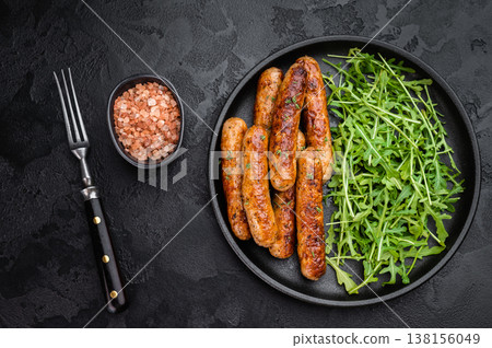 Fried sausage links with arugula greens on plate. Golden browned pork sausages served on dark textured background with copy space. 138156049