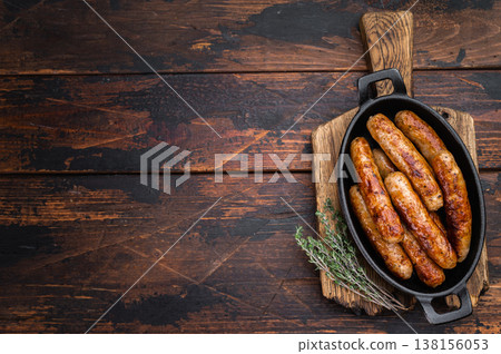 Grilled sausages in cast iron pan with thyme on rustic wooden table. Juicy browned pork meat links ready for dinner or barbecue with copy space. 138156053