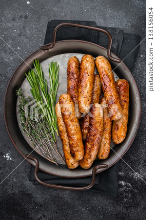Fried sausage links with herbs in metal pan over dark textured background. Golden browned pork sausages freshly cooked for meal. 138156054