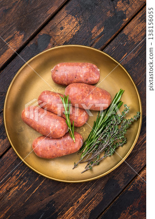 Raw pork sausage links with fresh herbs on rustic plate, traditional butcher style fresh meat product on wooden background. Raw pork sausage links with fresh herbs on rustic plate, traditional butcher style fresh meat product on wooden background. 138156055