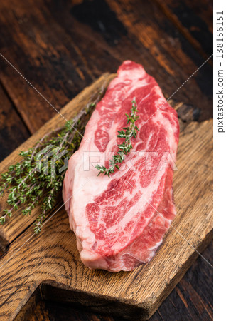 Raw beef chuck eye roll steak on wooden board with thyme and pepper. Marbled beef cut on dark wood background top view copy space.. 138156151