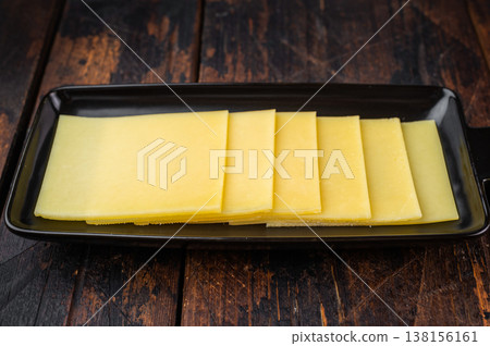 Square slices of mild creamy cheese on black plate, Gouda Edam type dairy product for sandwiches and cooking Square slices of mild creamy cheese on black plate, Gouda Edam type dairy product for sandwiches and cooking 138156161