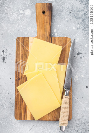 Stack of semi hard yellow cheese slices on rustic wooden cutting board, copy space on gray stone background, dairy ingredient Stack of semi hard yellow cheese slices on rustic wooden cutting board, copy space on gray stone background, dairy ingredient 138156163