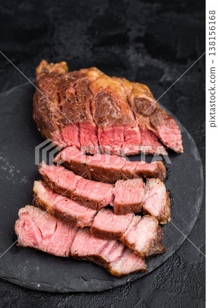 Sliced beef chuck eye roll steak cooked medium rare with juicy texture. Gourmet beef meat with salt on dark stone background. Sliced beef chuck eye roll steak cooked medium rare with juicy texture. Gourmet beef meat with salt on dark stone background. 138156168