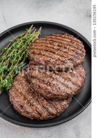 Grilled beef and lamb hamburger patties with seared crust in cast iron skillet. Cooked juicy meat on light stone background with copy space. 138156195