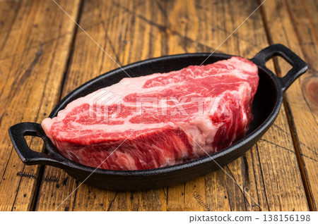 Uncooked beef chuckroll cut with rich marbling in skillet on wooden board. Fresh raw beef ingredient for grilling and cooking. Uncooked beef chuckroll cut with rich marbling in skillet on wooden board. Fresh raw beef ingredient for grilling and cooking. 138156198