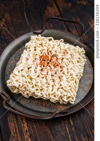 Square block of dry ramen noodles with spice powder and fresh herbs in metal pan on vintage wood background cooking ingredient scene 138156204