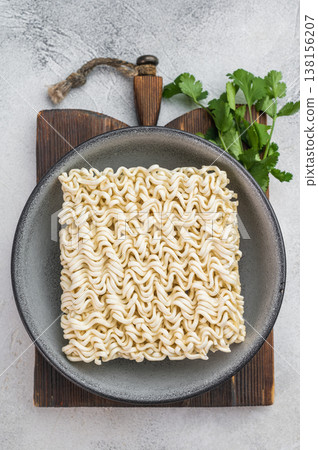 Raw wheat instant noodle brick in gray bowl on light surface with copy space minimal cooking ingredient flat lay. Raw wheat instant noodle brick in gray bowl on light surface with copy space minimal cooking ingredient flat lay. 138156207