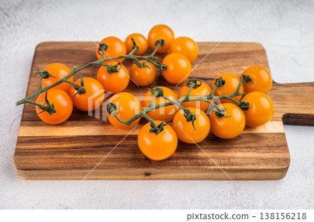 Yellow cherry tomatoes on vine on wooden cutting board over light textured background with copy space, fresh organic produce Yellow cherry tomatoes on vine on wooden cutting board over light textured background with copy space, fresh organic produce 138156218