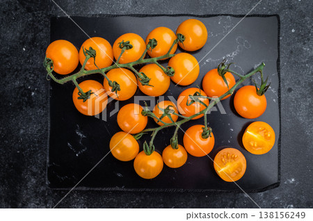 Organic orange cherry tomatoes whole and sliced on slate serving board, dramatic dark food composition with copy space Organic orange cherry tomatoes whole and sliced on slate serving board, dramatic dark food composition with copy space 138156249