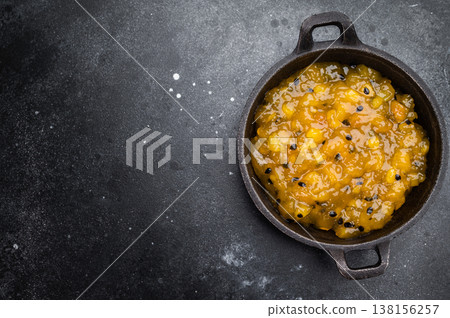 Mango and passion fruit sauce in cast iron pan on dark background, gourmet tropical fruit reduction with glossy texture 138156257