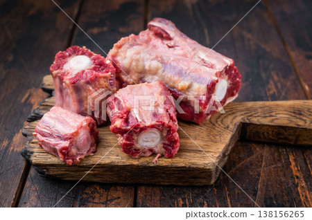 Lamb oxtail sections ready for cooking with herbs on wooden cutting board, overhead composition on dark wood surface Lamb oxtail sections ready for cooking with herbs on wooden cutting board, overhead composition on dark wood surface 138156265