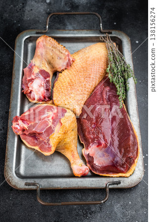 Uncooked duck breast and leg cuts on tray with herbs. Poultry game meat ingredient for cooking gastronomy overhead with copy space. 138156274