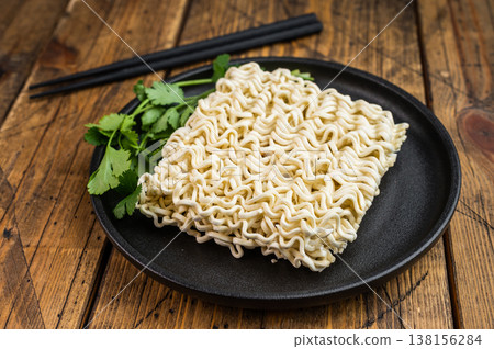 Raw wheat instant noodle brick with cilantro on black dish over vintage wood surface minimal Asian convenience food concept Raw wheat instant noodle brick with cilantro on black dish over vintage wood surface minimal Asian convenience food concept 138156284