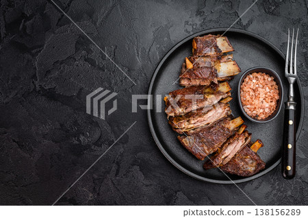 Roasted lamb ribs slab cut into portions with rich texture on dark stone background food photography Roasted lamb ribs slab cut into portions with rich texture on dark stone background food photography 138156289