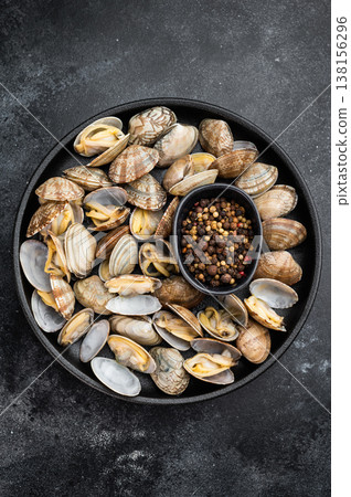 Cooked vongole clams served in cast iron skillet with spices on dark background. Italian seafood dish with open shells. Cooked vongole clams served in cast iron skillet with spices on dark background. Italian seafood dish with open shells. 138156296