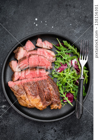 Seared beef chuck eye roll steak medium rare with fresh salad leaves. Restaurant style cooked beef on dark plate.. 138156301