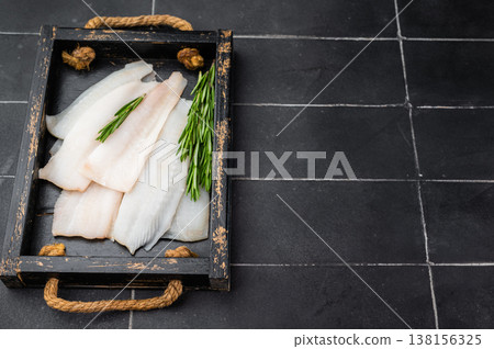 Raw hake or pollock fillets with rosemary on rustic wooden tray. Fresh cod whitefish meat for cooking seafood meals on dark kitchen background. Raw hake or pollock fillets with rosemary on rustic wooden tray. Fresh cod whitefish meat for cooking seafood meals on dark kitchen background. 138156325