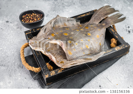 Whole flounder flatfish with spotted skin on rustic tray with pepper on light background fresh raw seafood 138156336