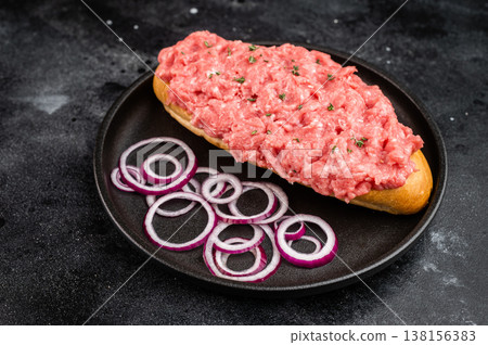 Raw beef cannibal sandwich with minced beef and red onion served on bread roll on black plate Raw beef cannibal sandwich with minced beef and red onion served on bread roll on black plate 138156383