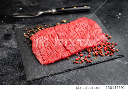 Raw beef flank steak bavette style with strong muscle grain on slate plate with peppercorns on dark background Raw beef flank steak bavette style with strong muscle grain on slate plate with peppercorns on dark background 138156391
