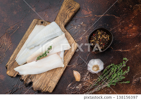 Raw cod or hake fillets with thyme on wooden board and pepper on dark textured background. Fresh pollock whitefish prepared for healthy seafood cooking. 138156397
