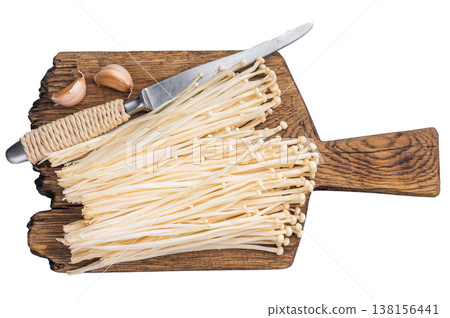Raw Enoki mushrooms, garlic, and a knife on a rustic wooden cutting board. Kitchen preparation and healthy cooking concept. Raw Enoki mushrooms, garlic, and a knife on a rustic wooden cutting board. Kitchen preparation and healthy cooking concept. 138156441