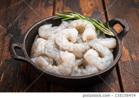 Raw peeled shrimp prawn and rosemary in a dark cast iron skillet on a rustic wooden background. Top view with copy space for recipe or menu. 138156454